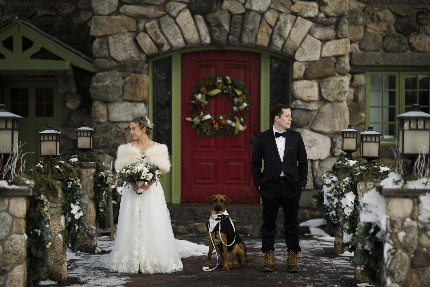 A bride and groom with their dog outside a mansion