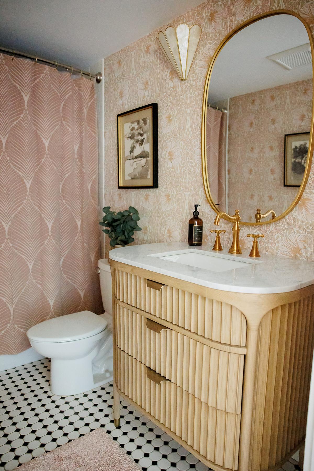 Bathroom with pink shower curtain, gold accents, and wood vanity.