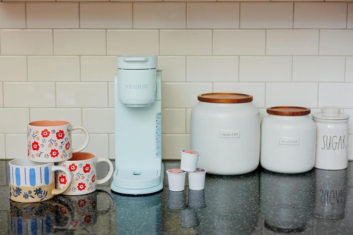 Coffee machine with mugs, canisters, and coffee pods on a kitchen counter.