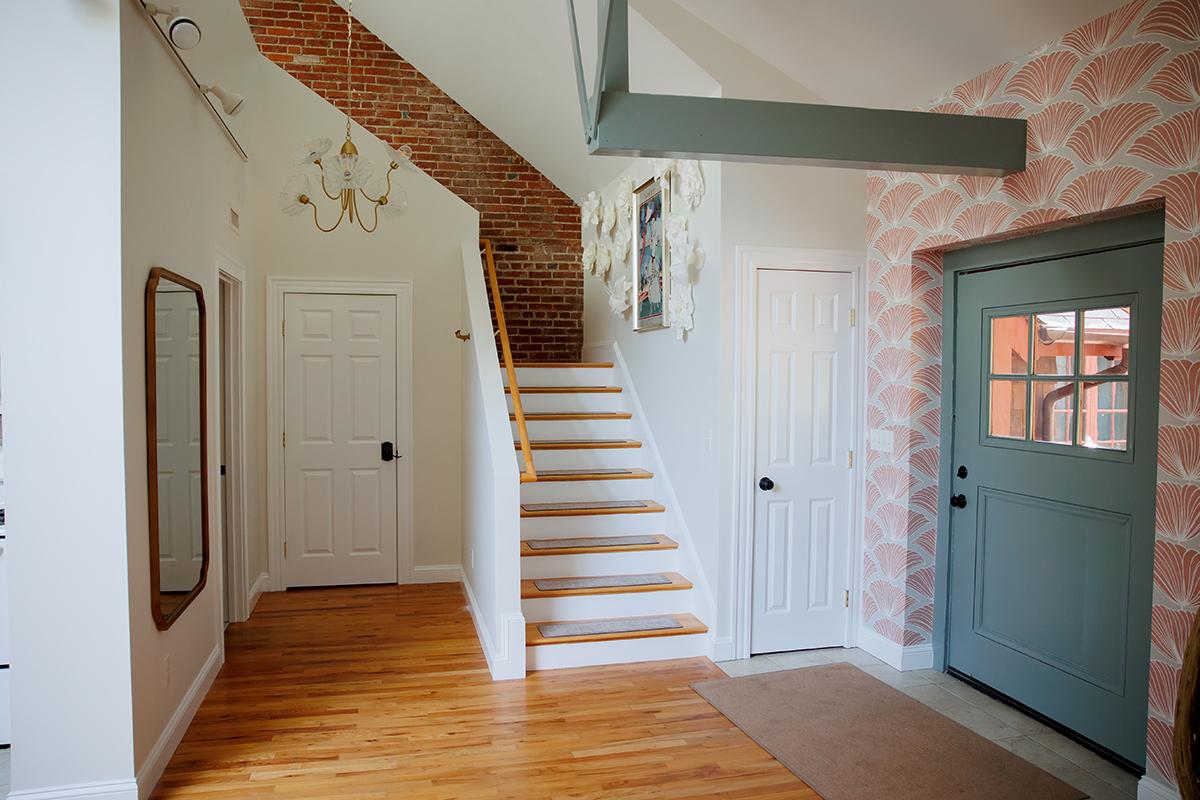 Bright foyer with wooden floors, staircase, chandelier, and light blue front door.