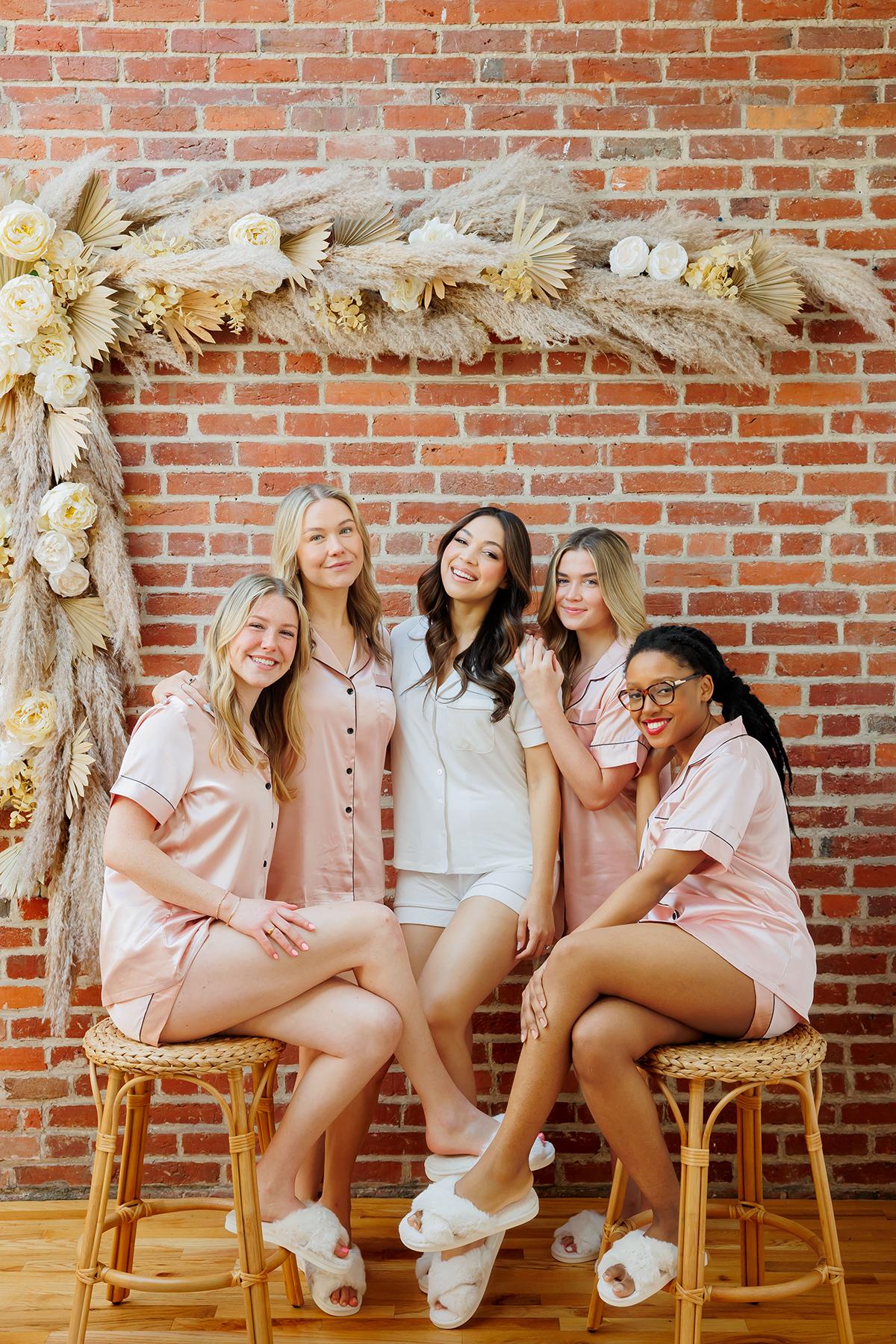 Group of women in pajamas posing against brick wall with floral decoration.