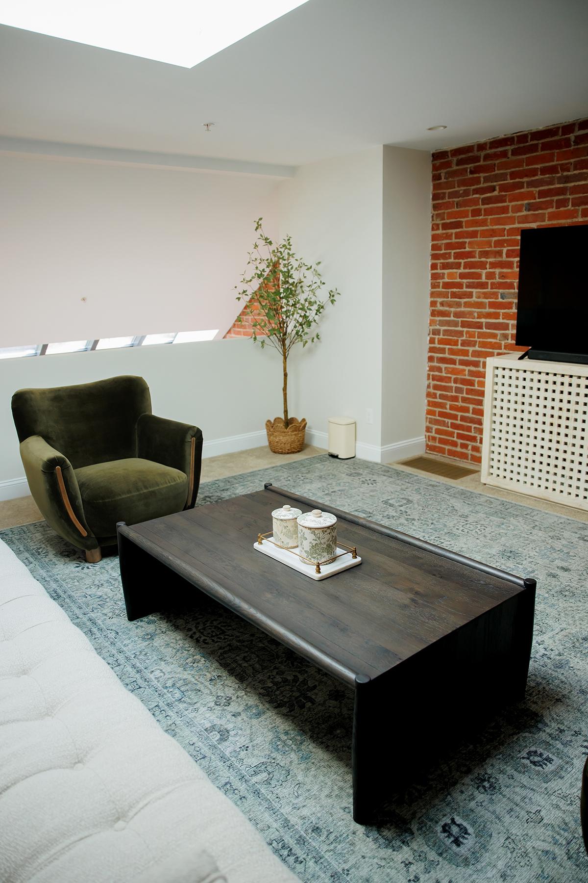 Cozy living room with a green armchair, dark coffee table, and a brick accent wall.