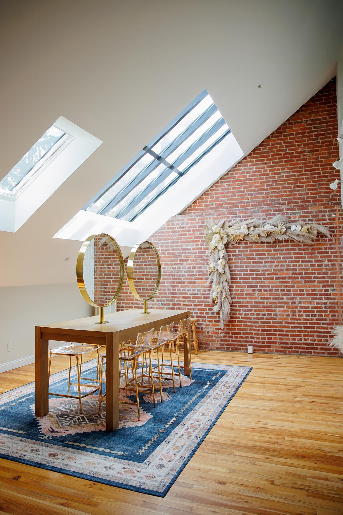 Modern room with wooden table, chairs, brick wall, skylights, and blue rug.