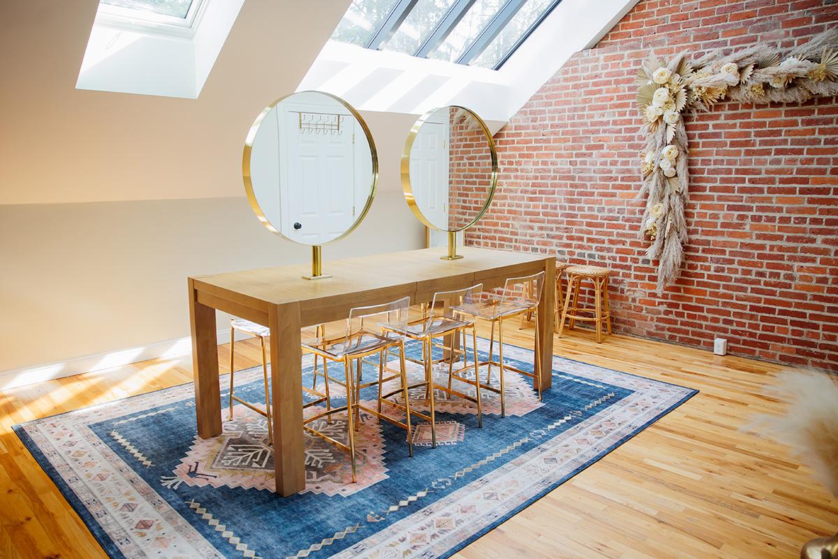 Bright room with wooden table, round mirrors, and skylights. Brick wall decor.