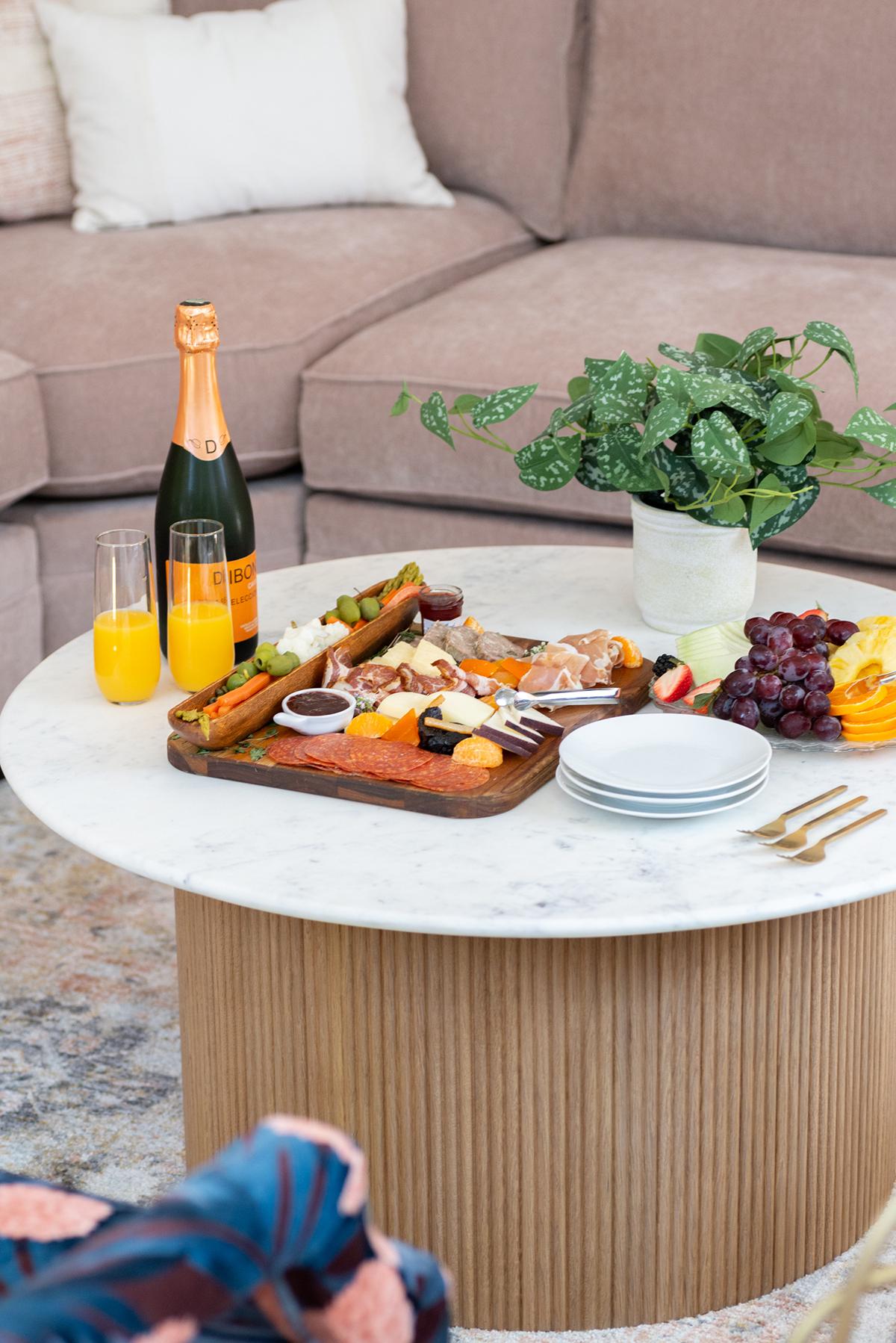 Charcuterie board on a marble table with drinks, near a sofa.