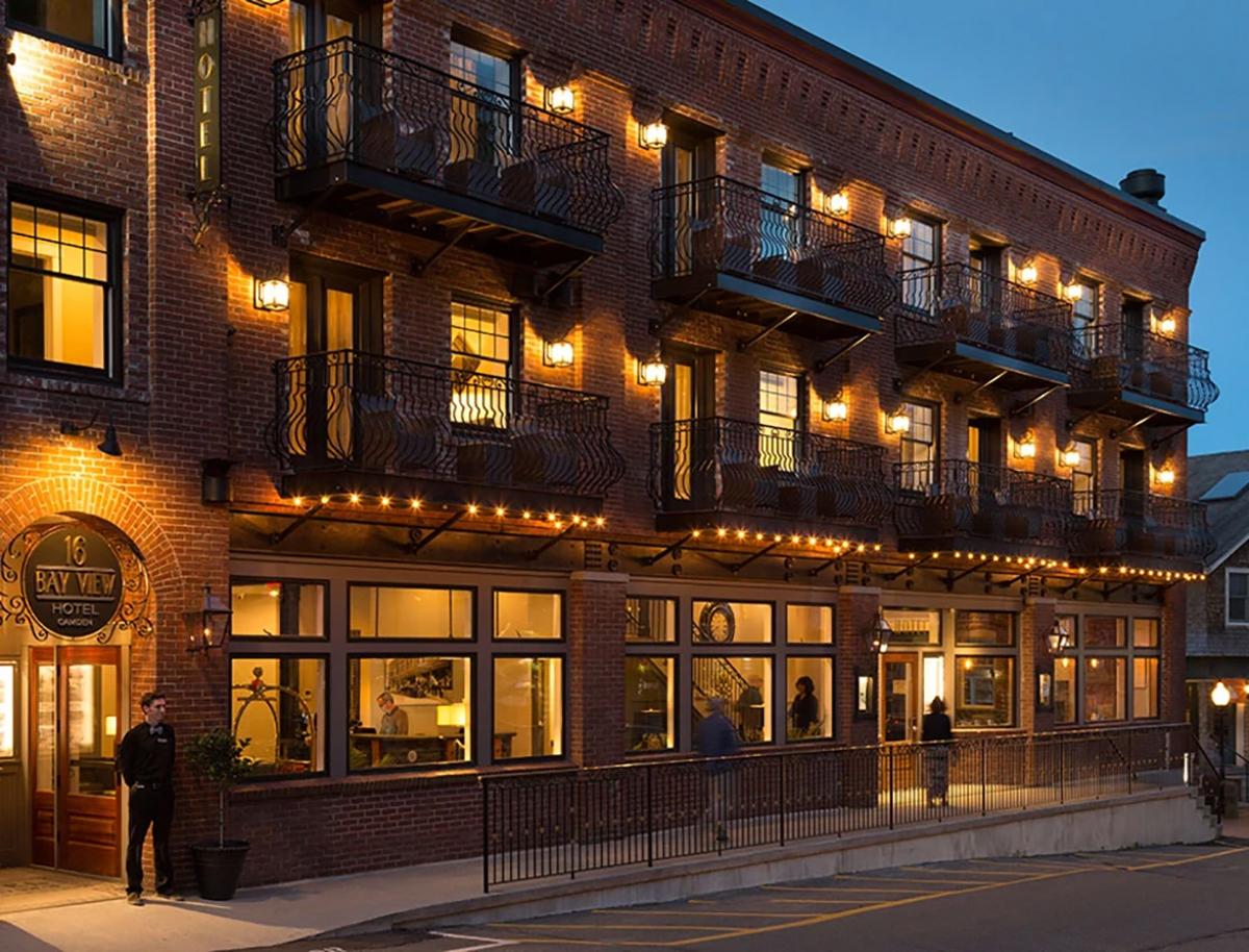 Historic brick hotel at dusk, warmly lit, with balconies and street below.
