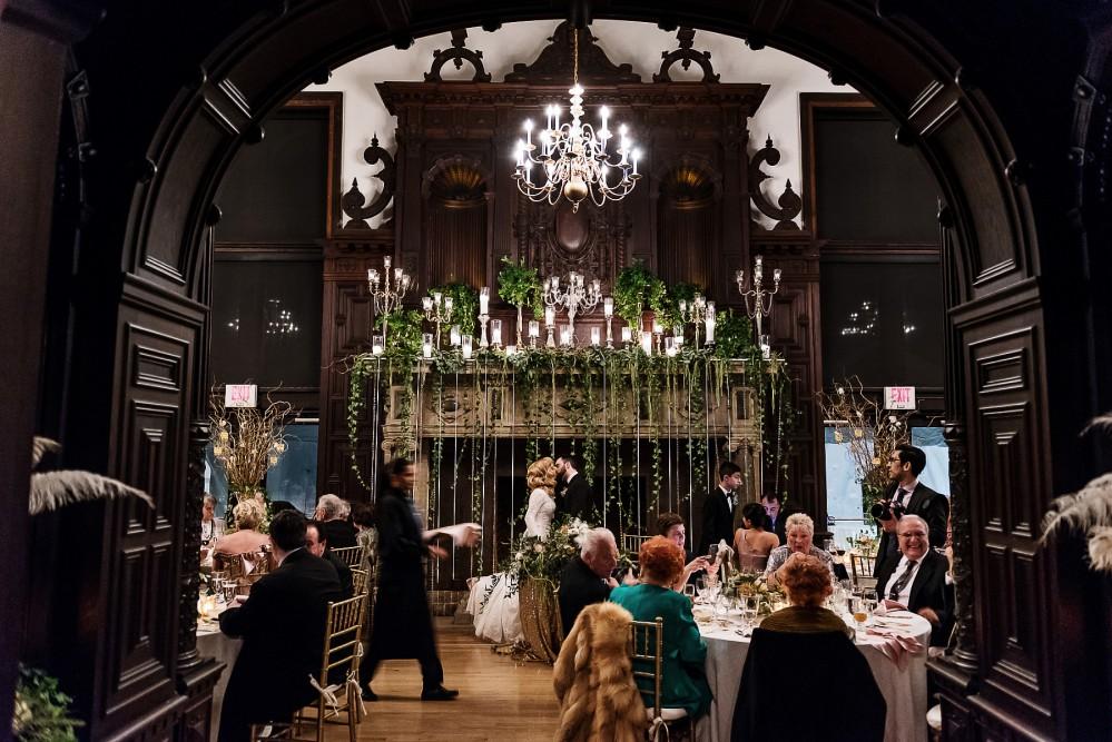 Opulent dining room with guests seated, ornate chandelier, and floral decorations.