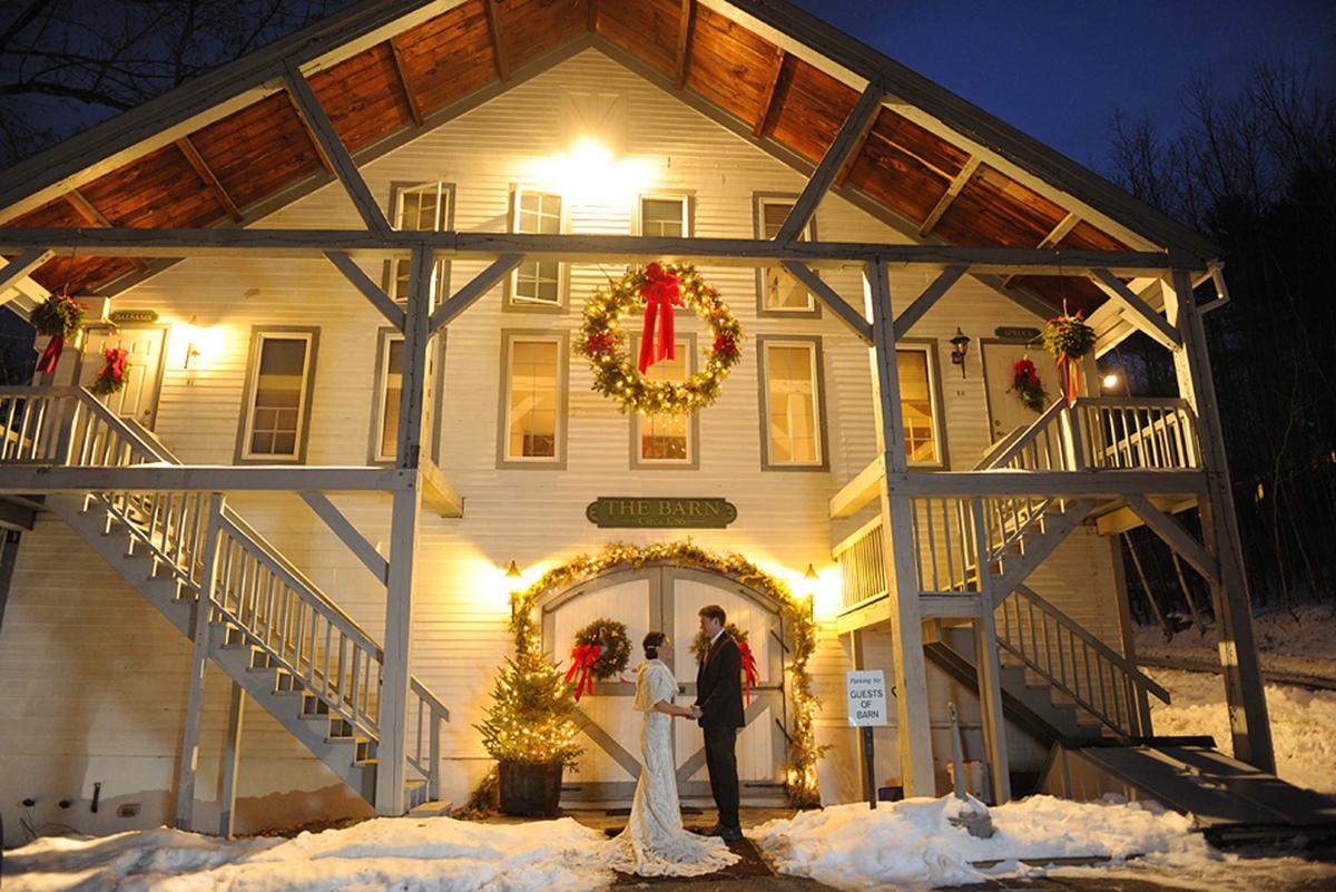 Bride and groom stand outside a warmly lit house decorated with wreaths at night.