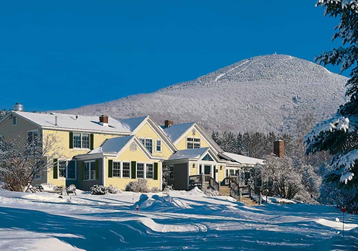 Yellow house in snowy landscape with blue sky and mountain in the background.