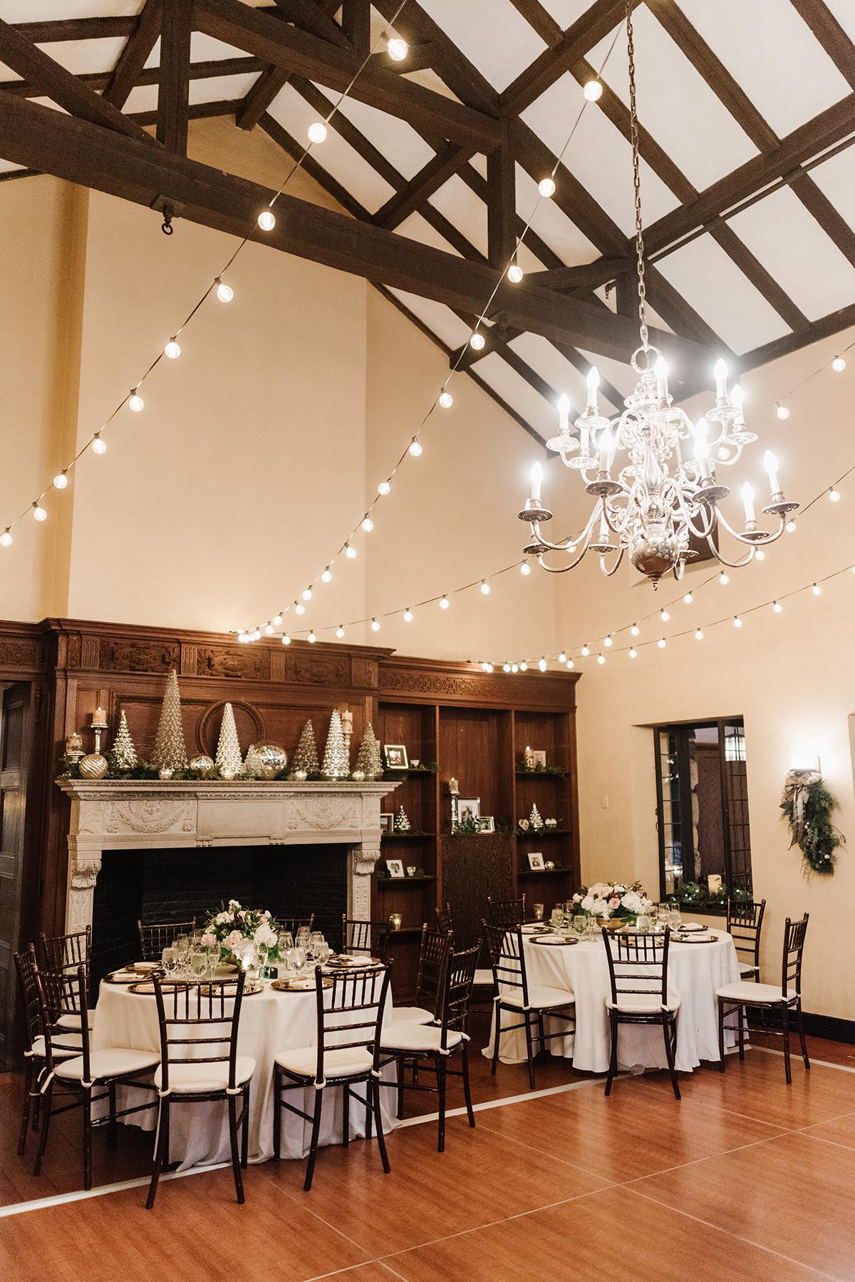 Elegant dining room with fireplace, chandeliers, and string lights.