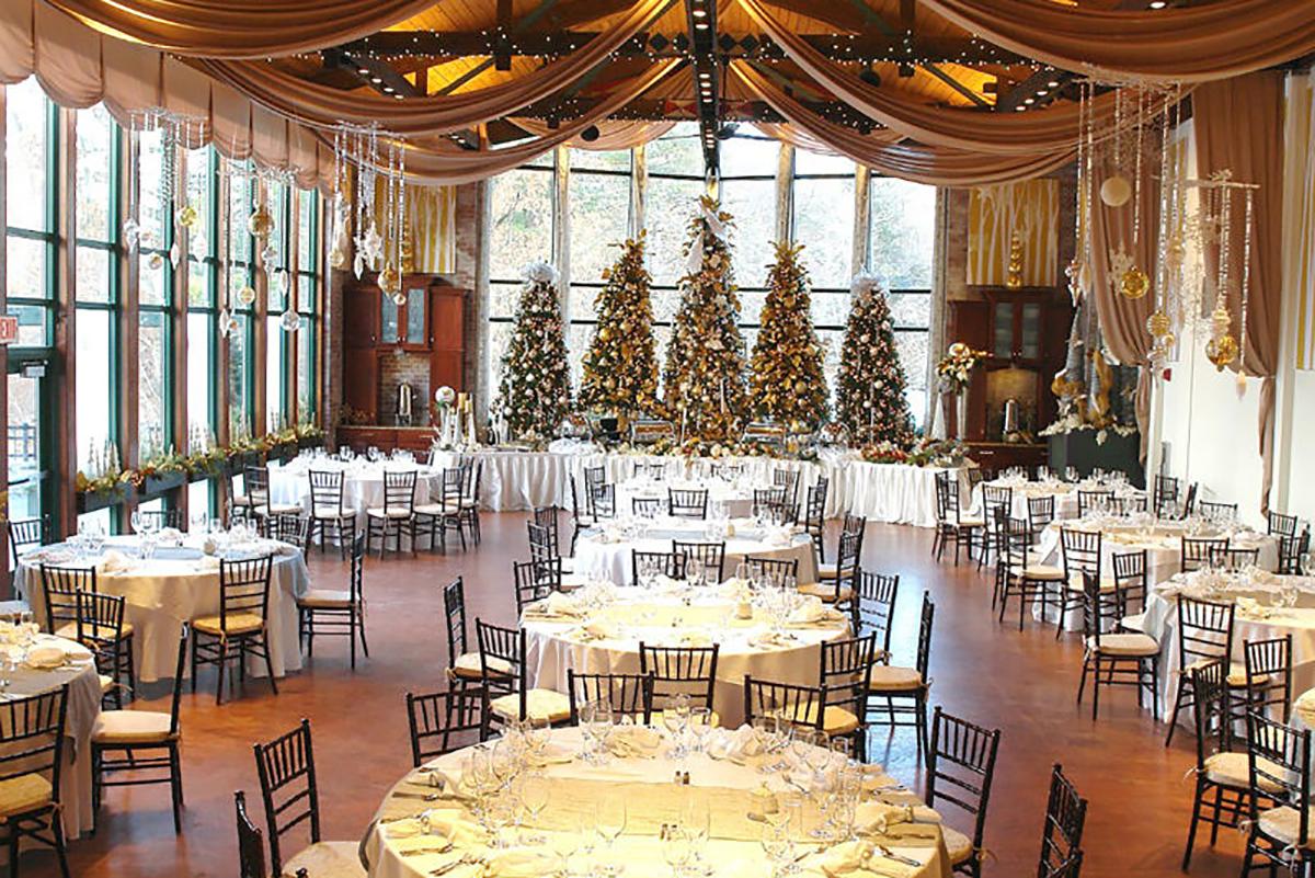 Elegant banquet hall with decorated Christmas trees and round tables set for dining.