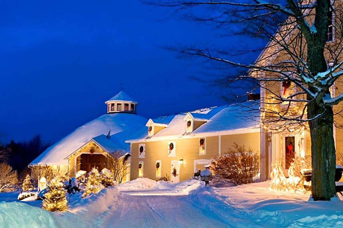 Snow-covered house with warm lights at night, under a deep blue sky.