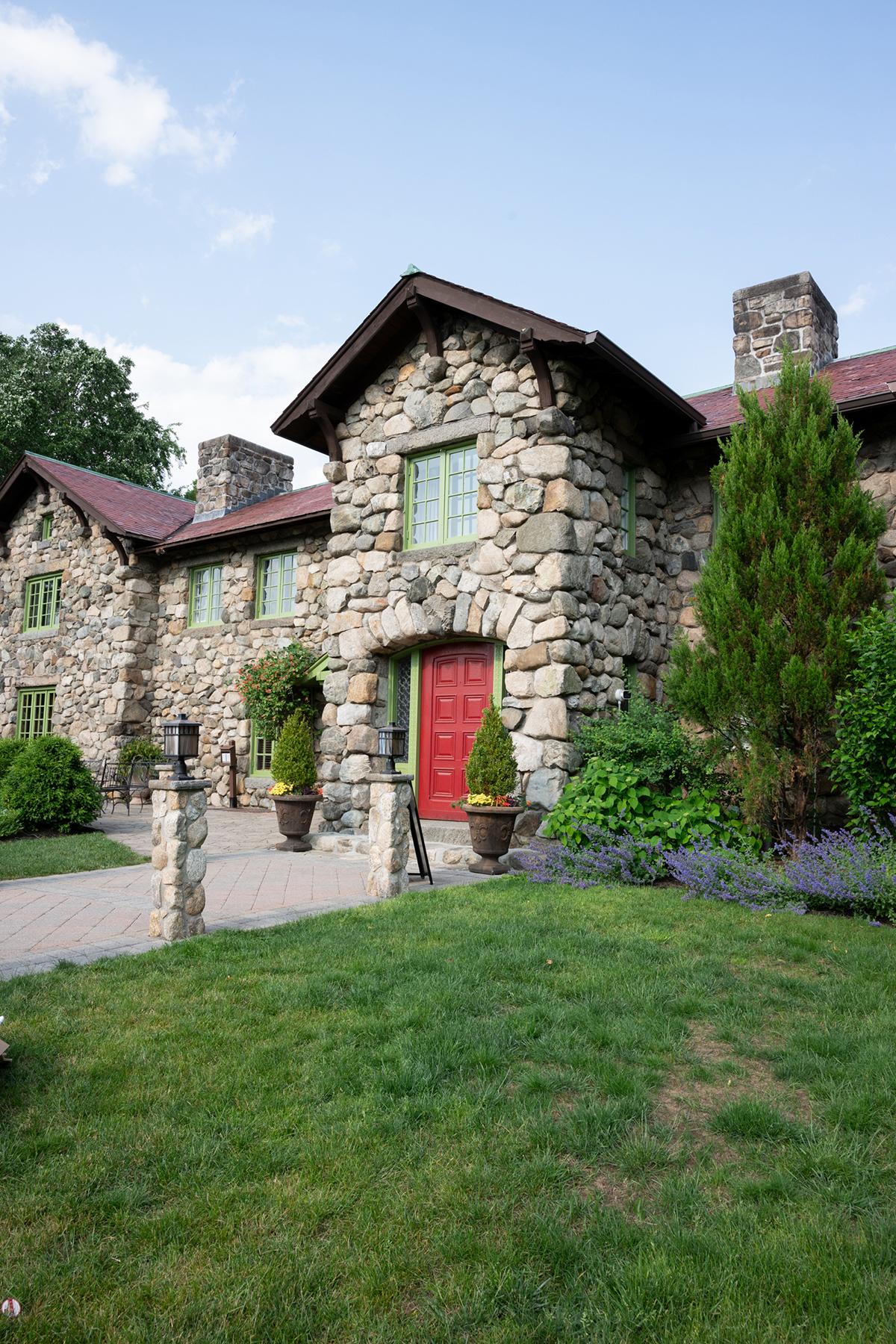 Stone house with red door, surrounded by greenery and a manicured lawn.