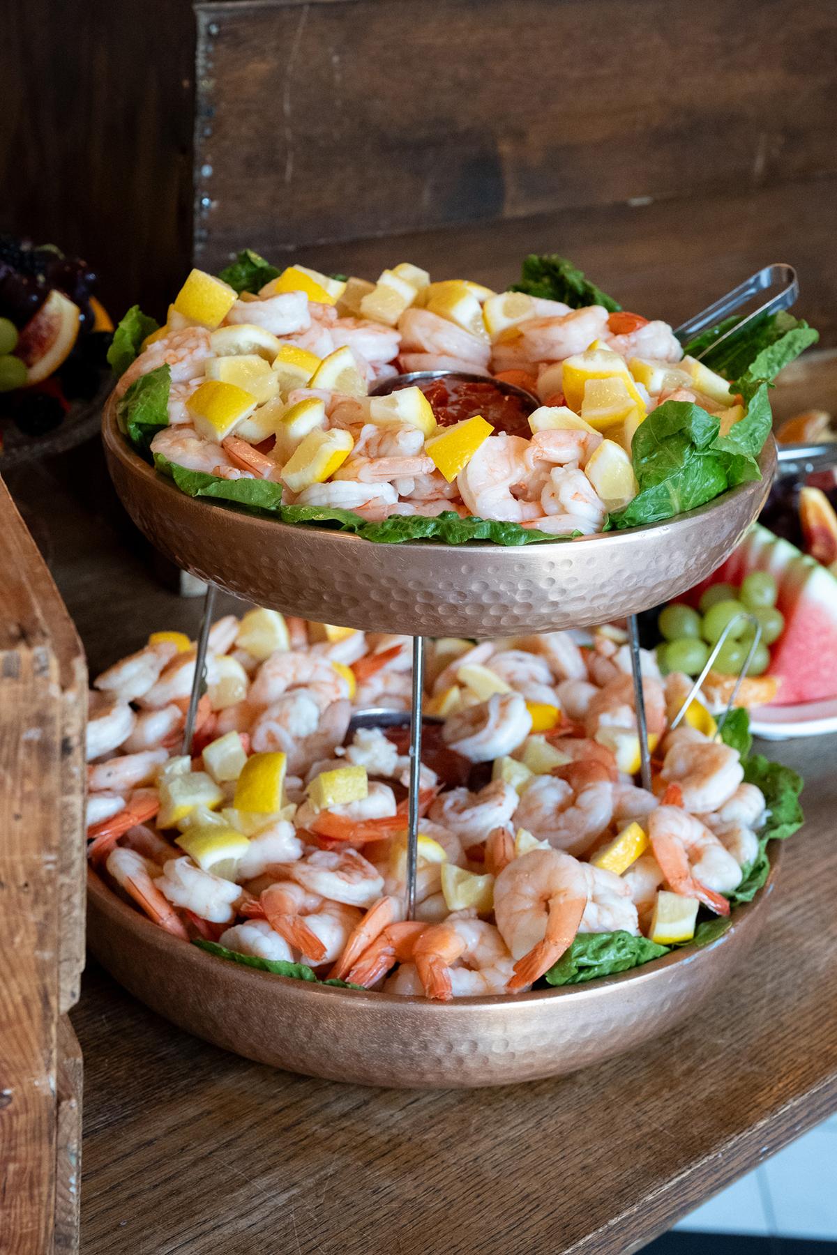 Two-tiered tray with shrimp salad and mango pieces.