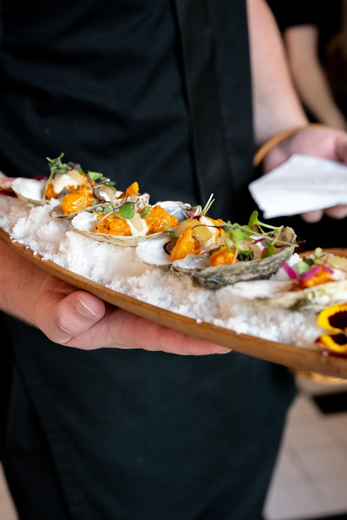 Oysters served on a wooden tray, garnished with herbs.