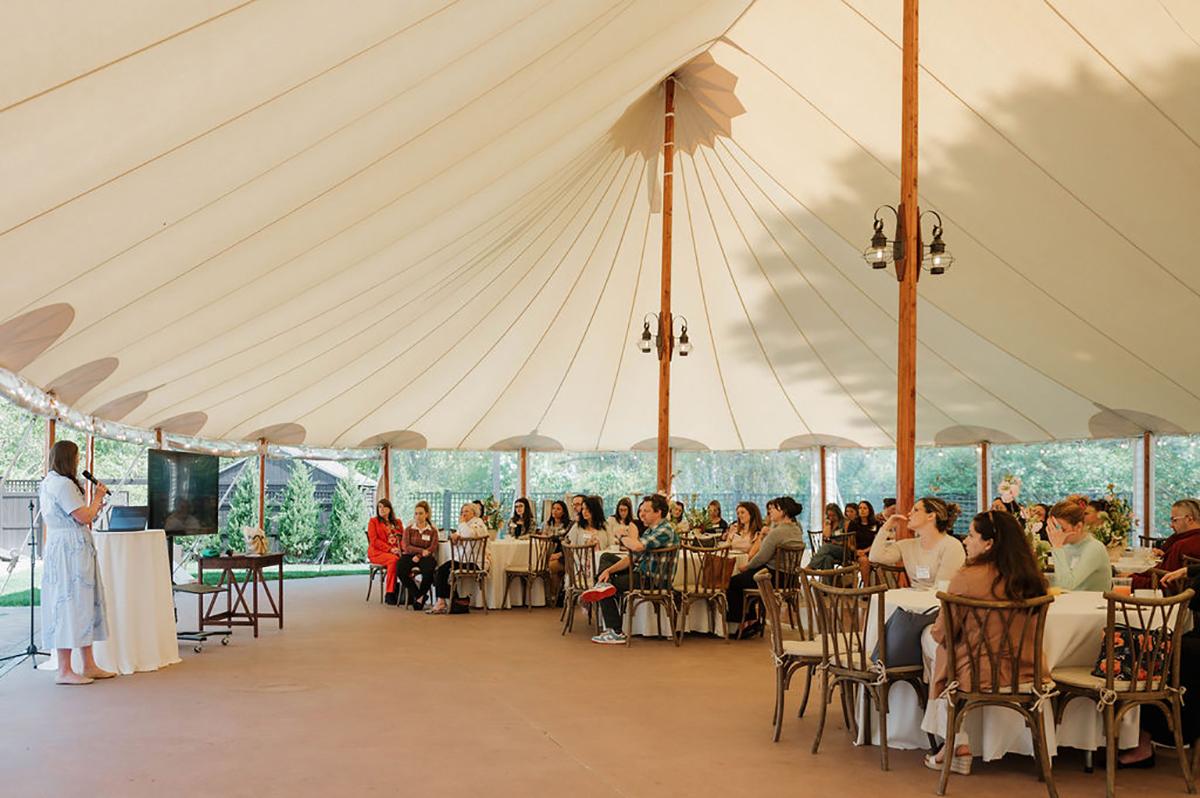 Speaker addresses guests under a large white tent.