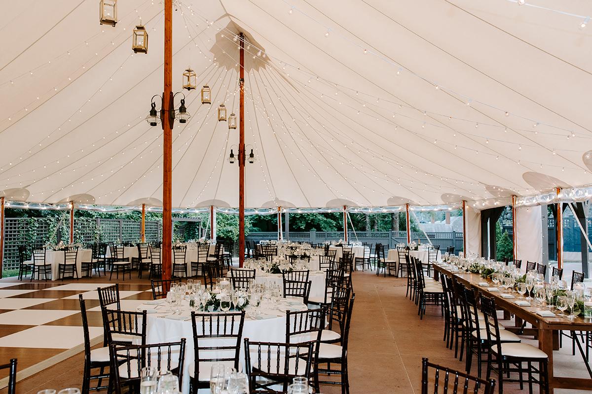 Elegant banquet hall with round tables, white canopy, and wooden chiavari chairs.