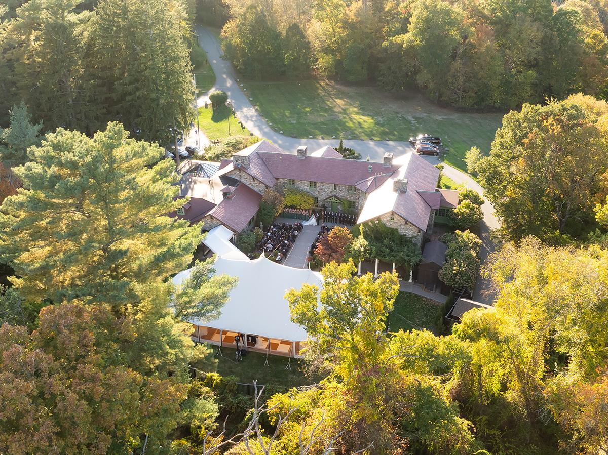 Aerial view of a large house surrounded by autumn trees and a winding path.