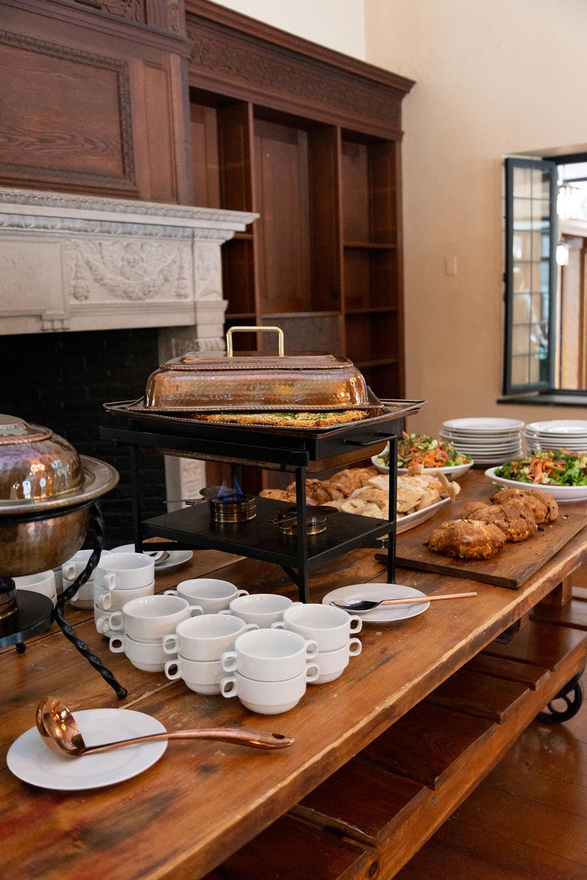 Buffet table with pastries, salads, and stacked cups in a cozy room.
