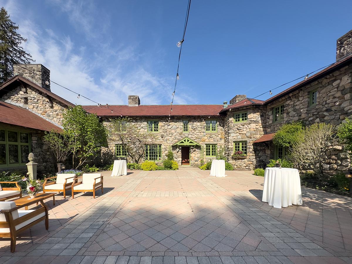 Stone courtyard with tables, chairs, and a clear blue sky.