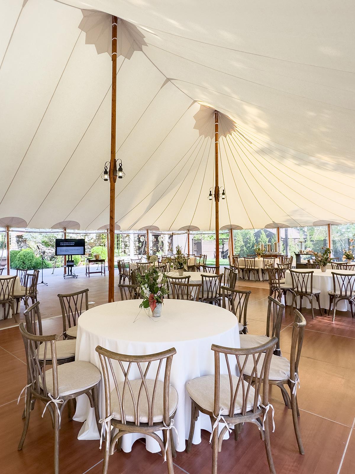 Wedding reception tent with round tables and elegant chairs.
