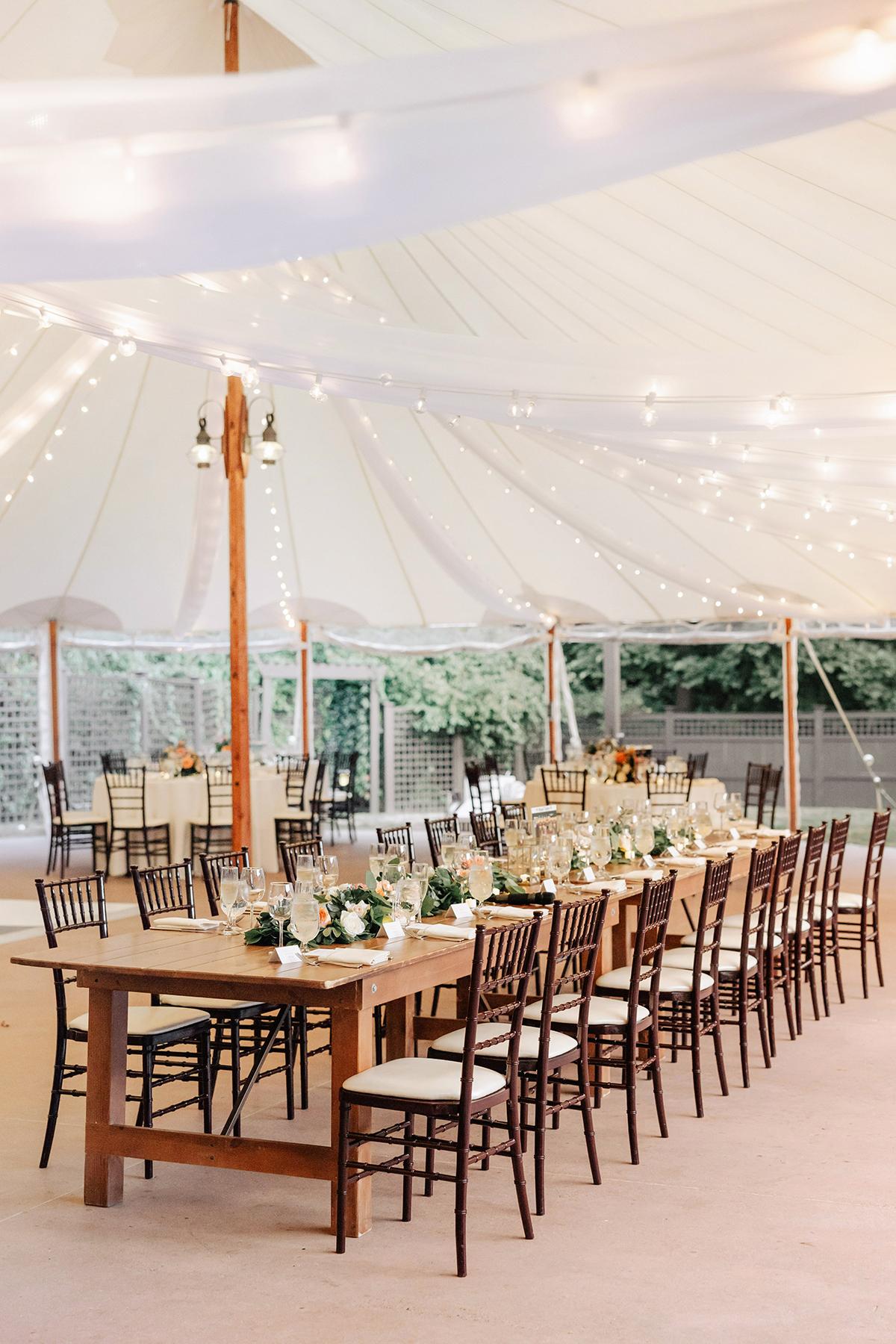 Elegant wedding reception with long tables, under a white tent with string lights.
