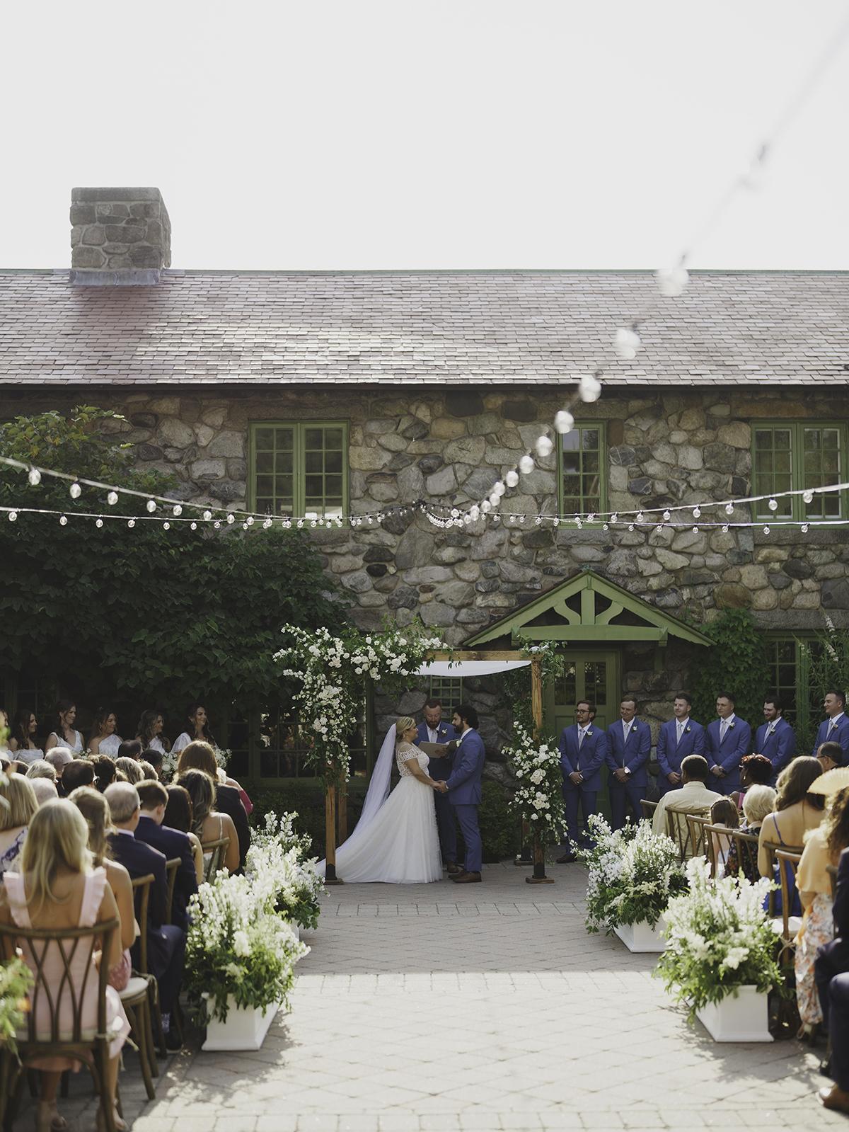 Wedding ceremony outside a stone house under string lights.