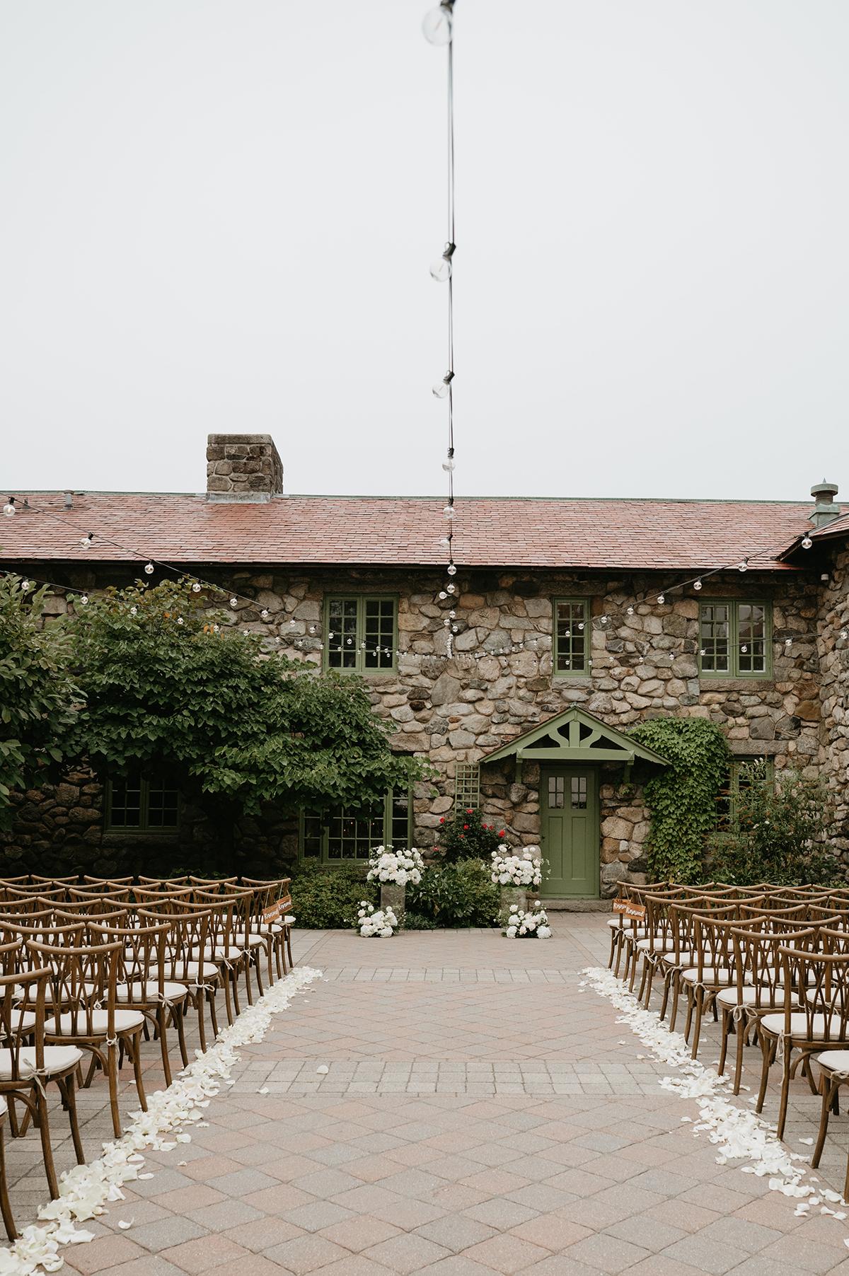 Outdoor wedding setup with chairs facing a stone building.