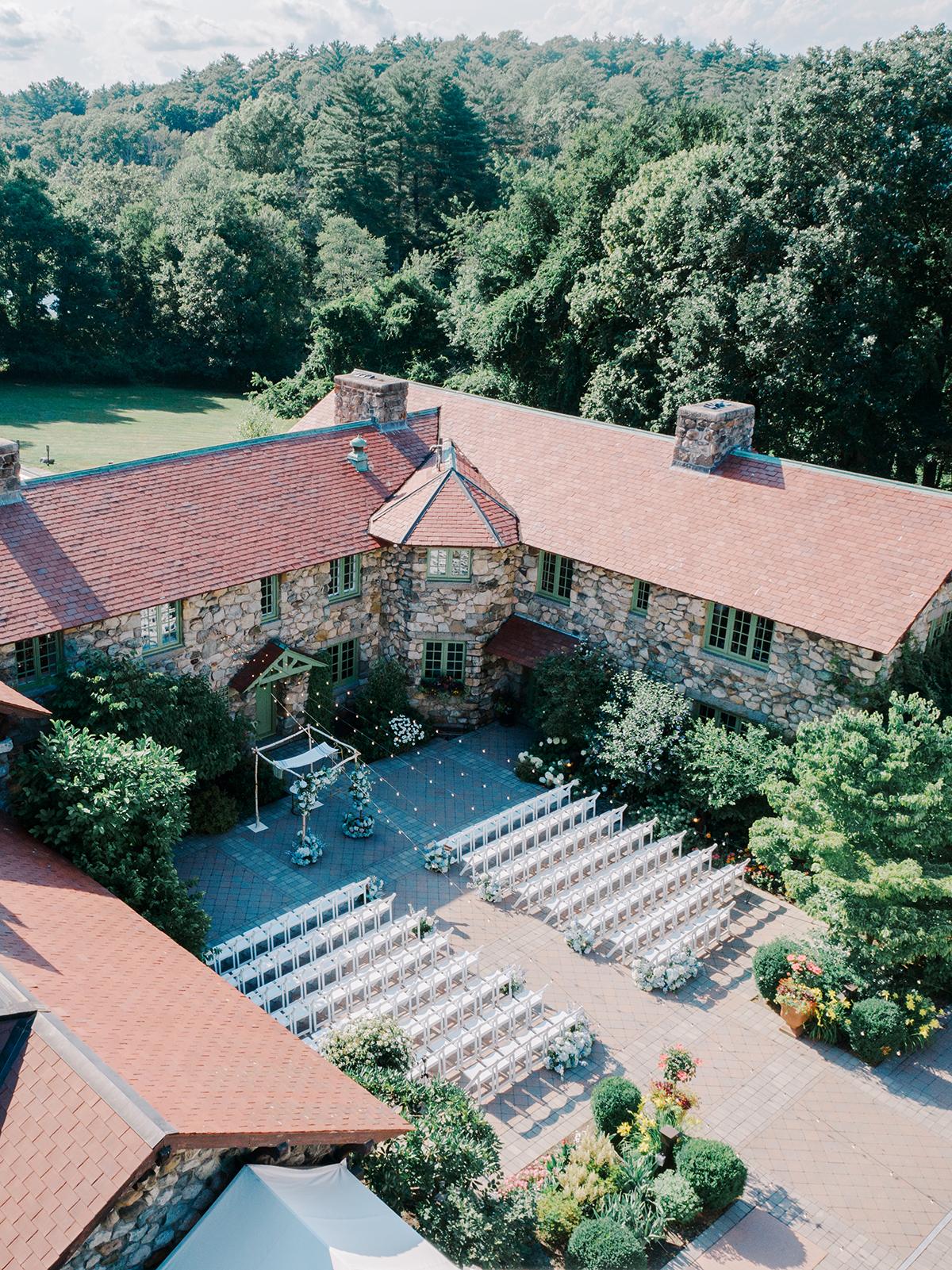 Courtyard wedding setup with chairs, surrounded by trees and a rustic stone building.