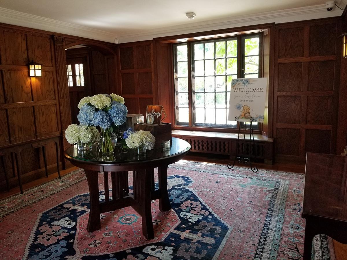 Room with wooden walls, table with blue and white flowers, and large window.