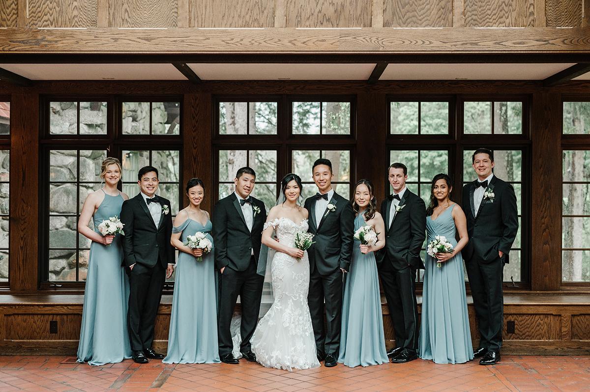 Wedding party with bridesmaids in blue dresses, groomsmen in dark suits, and a couple in the center.