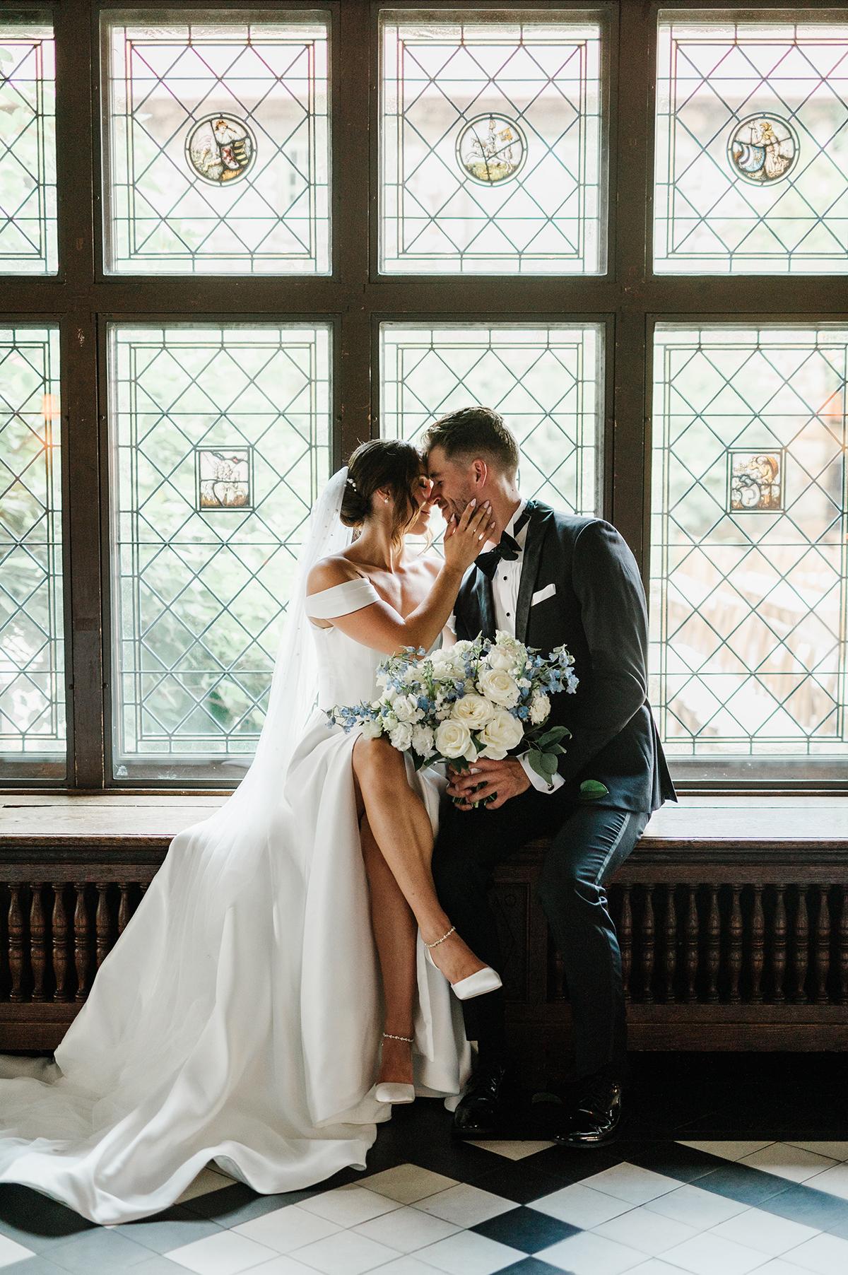 Bride and groom sitting together, sharing an intimate moment by stained glass windows.