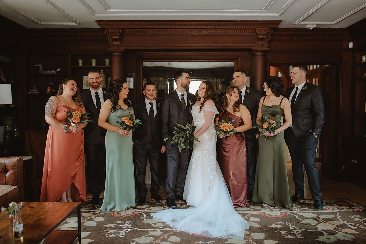 Wedding party in formal attire, standing together and smiling indoors.