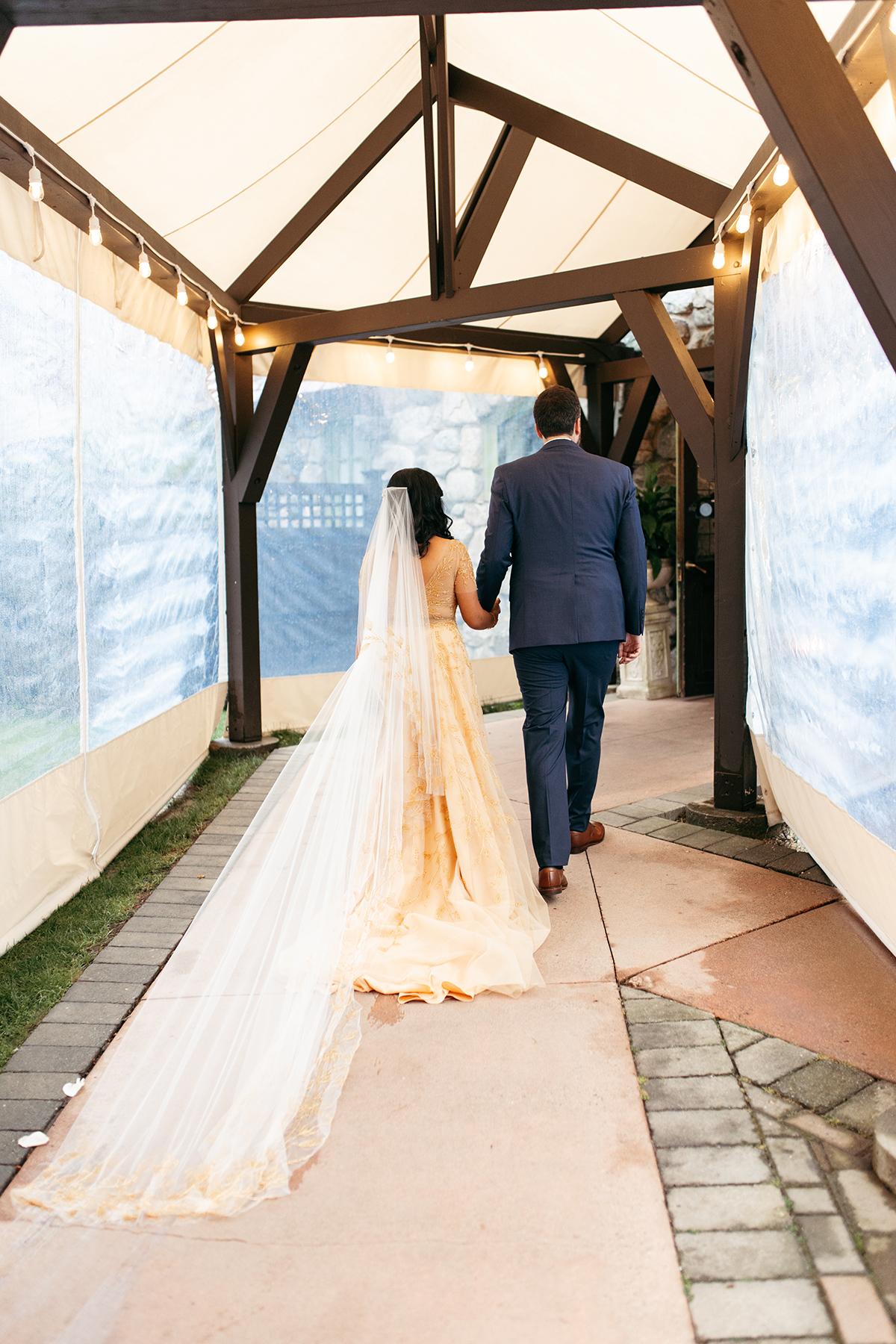 Bride and groom walking hand-in-hand under a canopy.