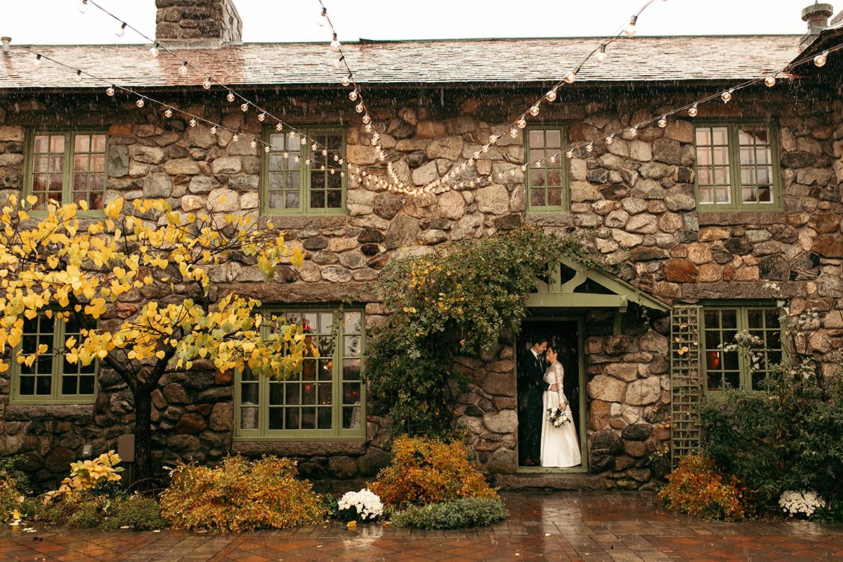 Stone cottage with ivy and autumn leaves, a person stands in the doorway.