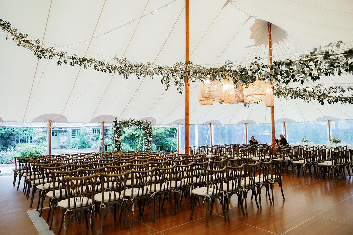 Wedding venue under a tent with rows of chairs and greenery.