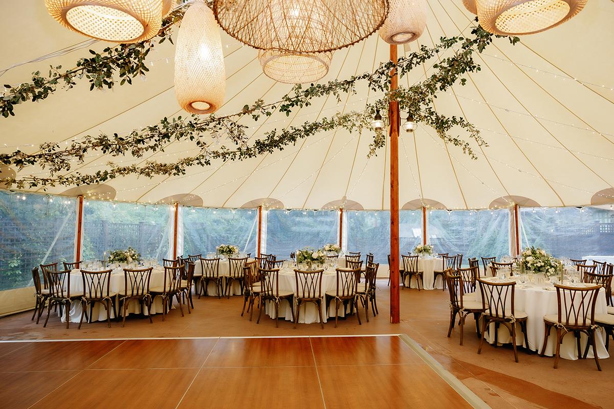 Elegant wedding tent with round tables, white linens, and floral centerpieces.