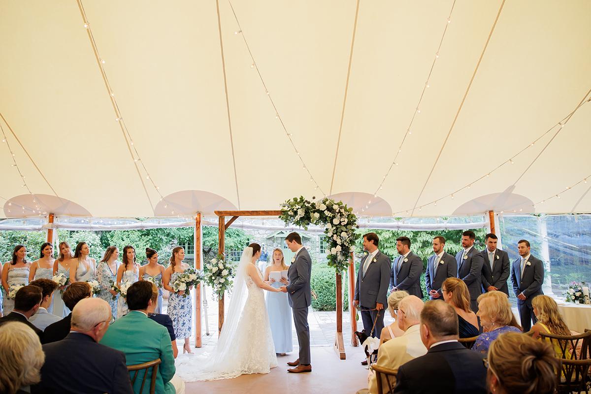 Couple exchanging vows under floral arch at outdoor wedding ceremony.