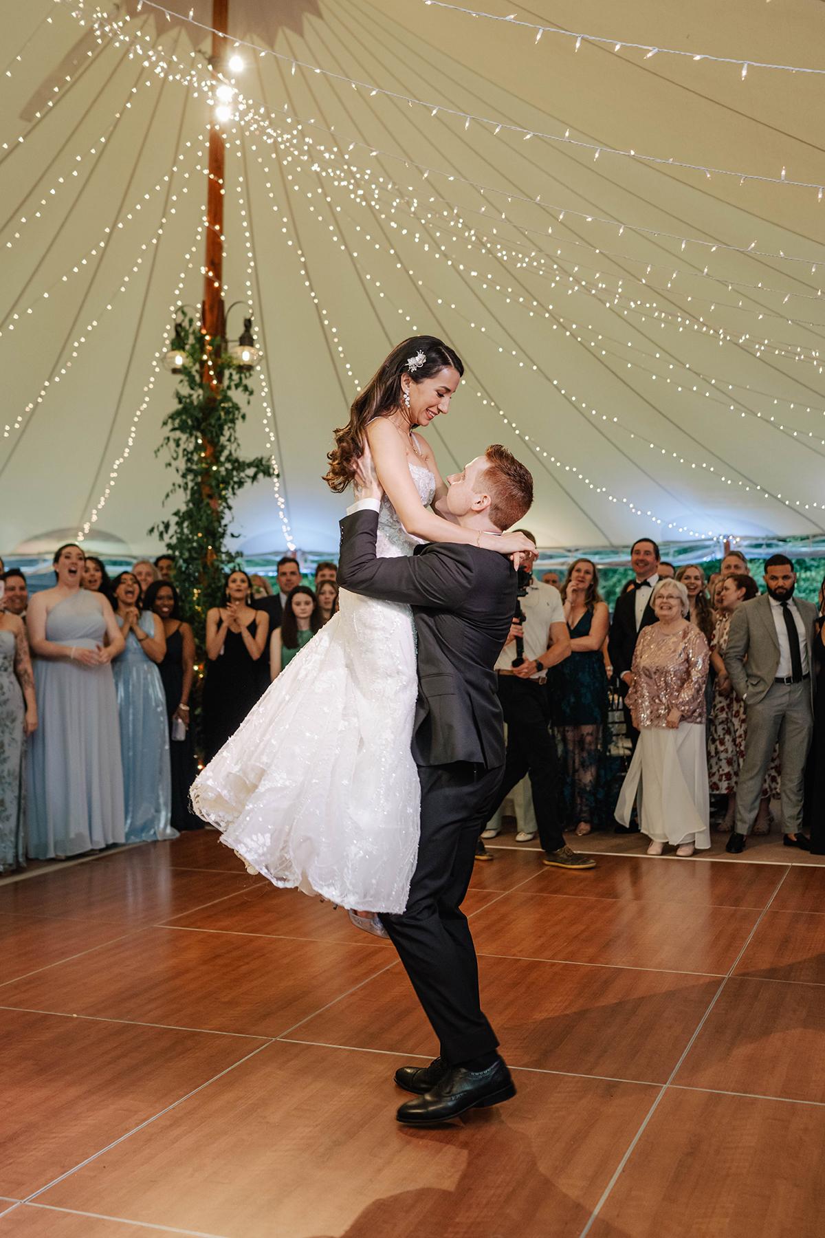 Bride and groom dancing under string lights, surrounded by guests.