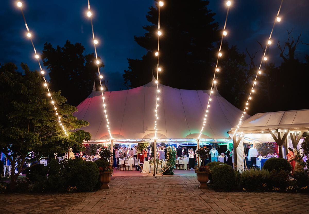 Nighttime garden party under a tent with string lights and guests mingling.