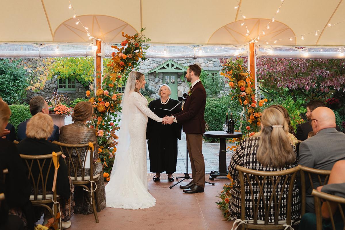 Wedding ceremony under a decorated tent with guests seated.