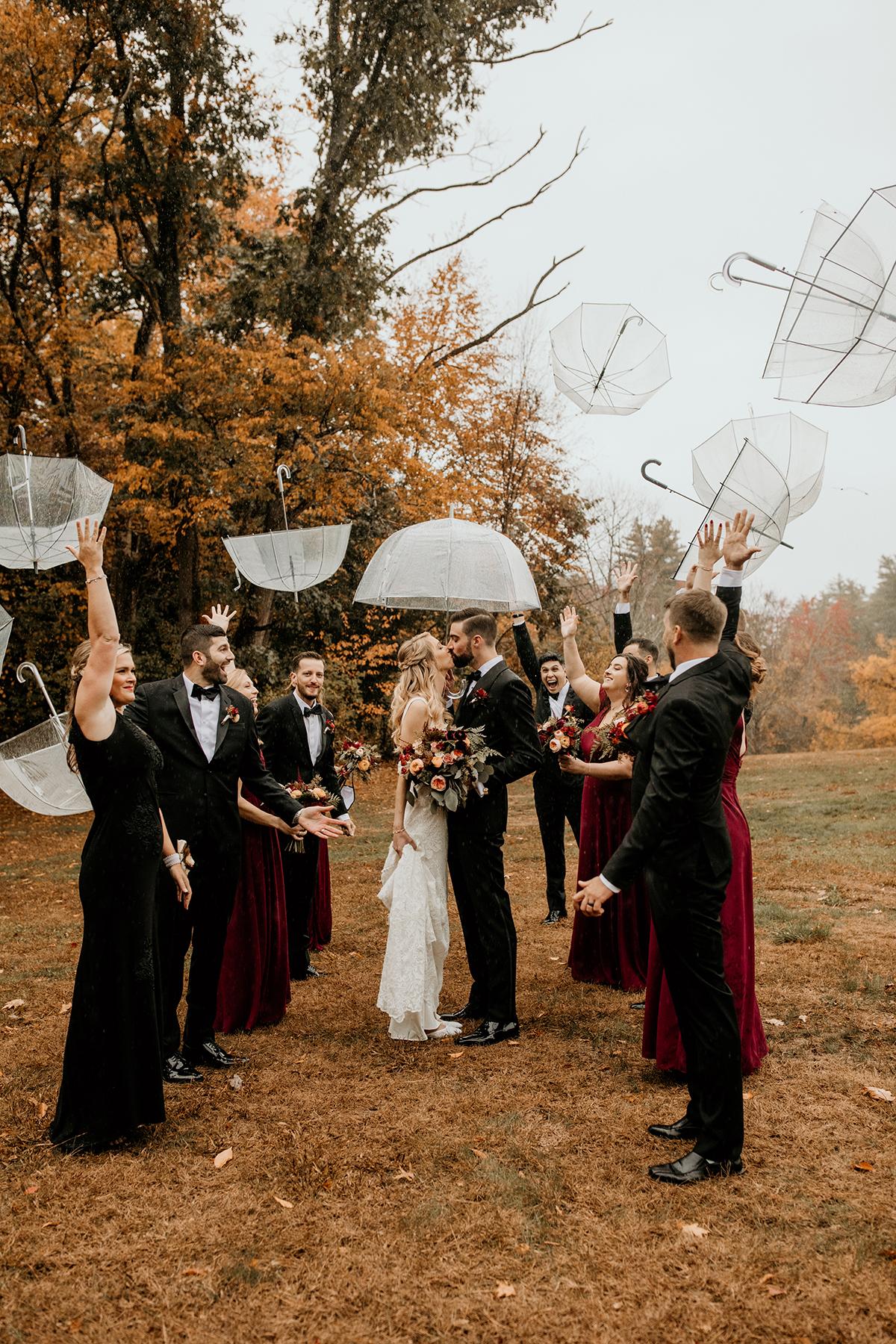 Wedding party under clear umbrellas, surrounded by autumn trees.