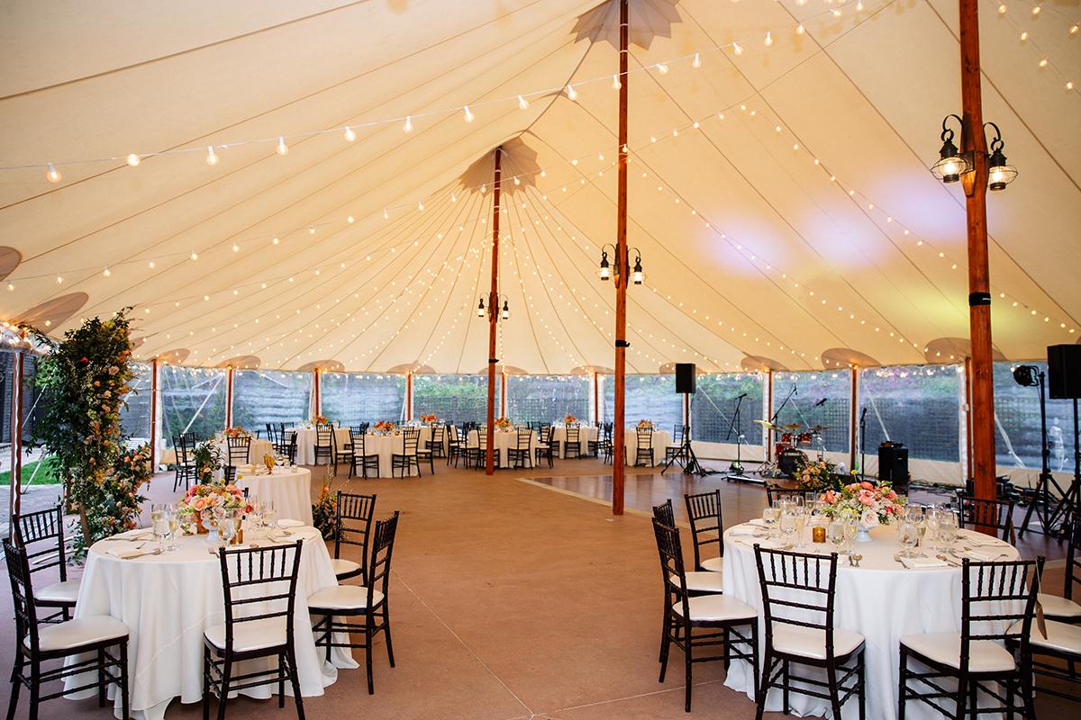 Wedding reception tent with round tables, white linens, and string lights.