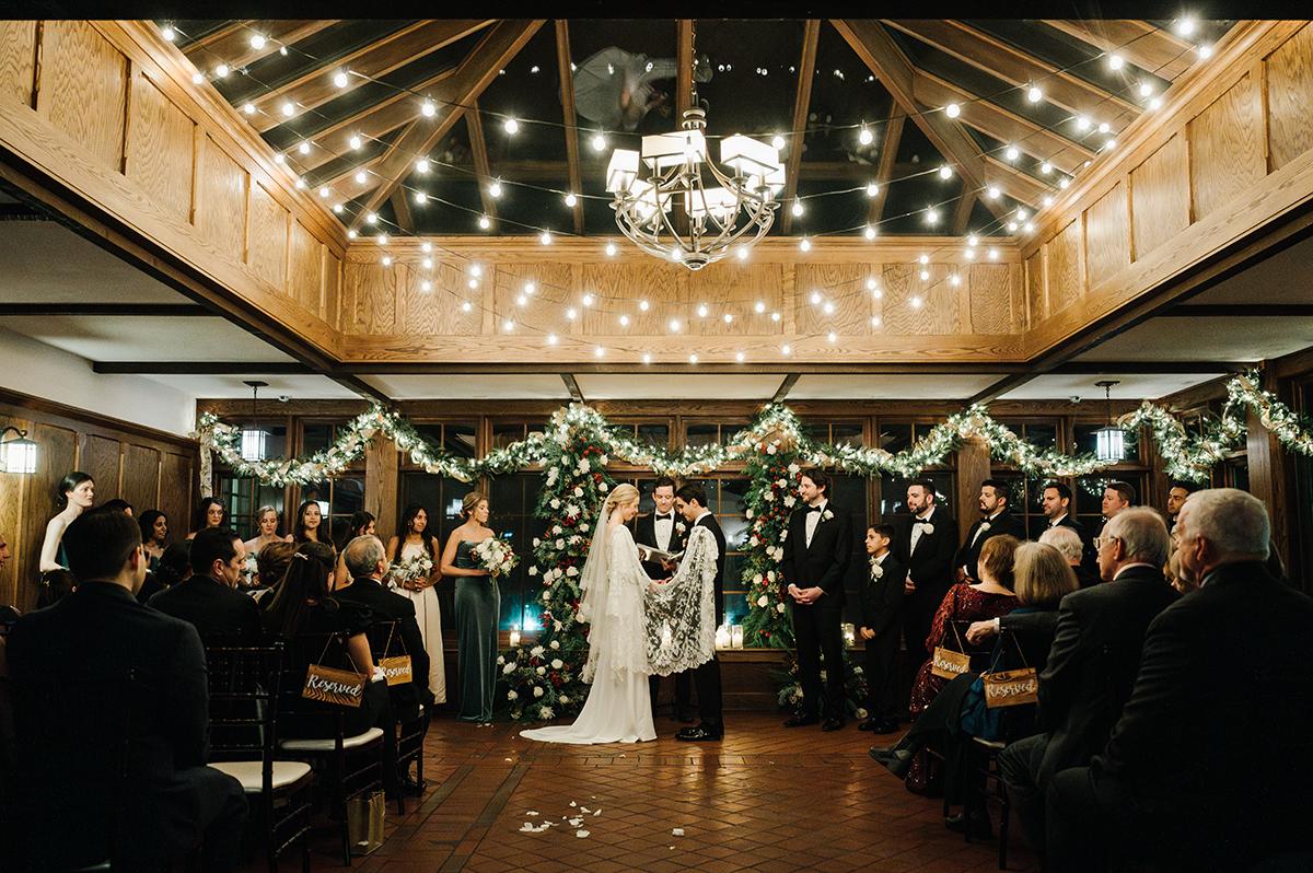 Wedding ceremony with lights and garlands, couple stands at the altar, guests seated.