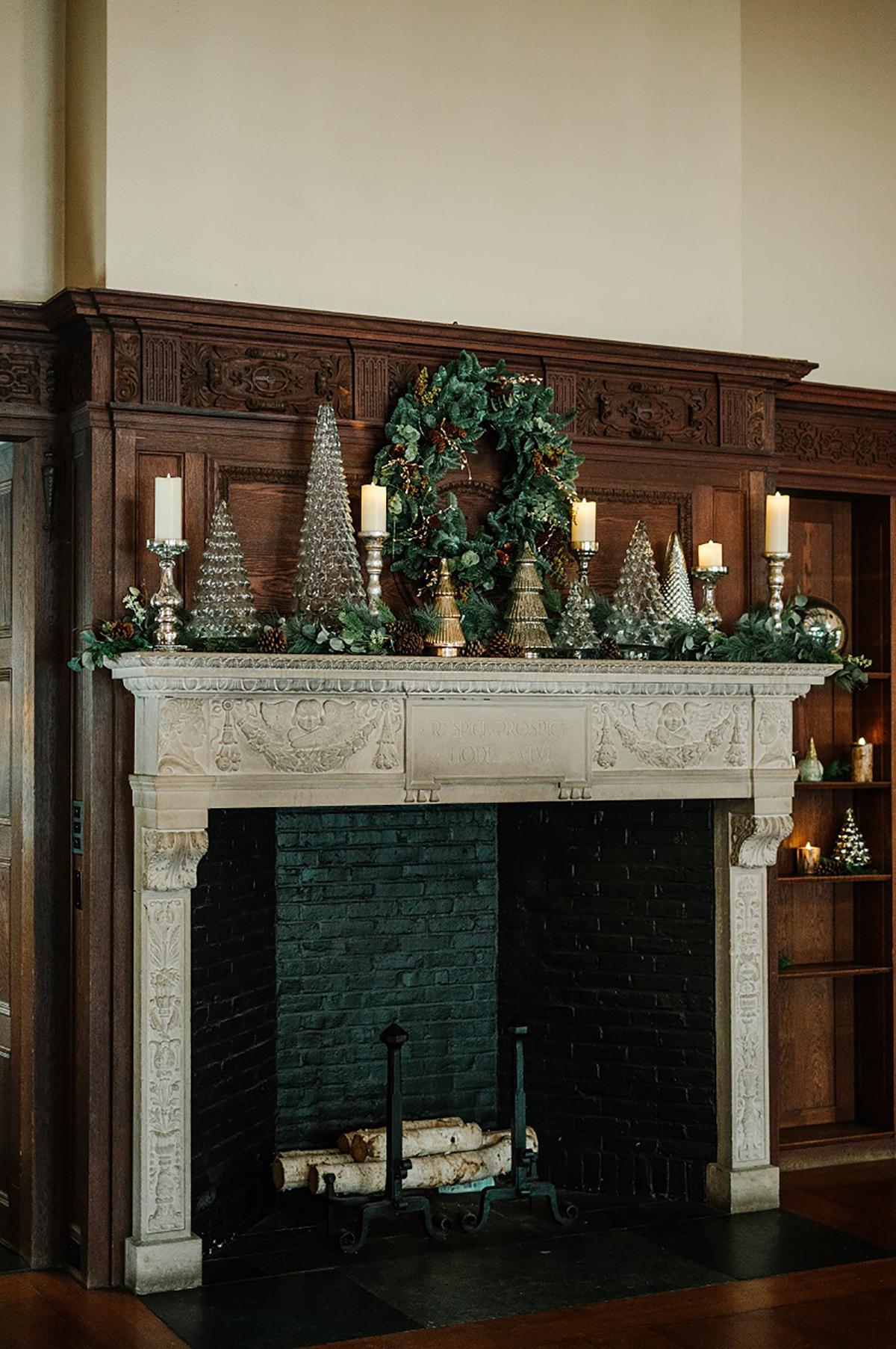 Festive fireplace with wreath, candles, and decorative trees.