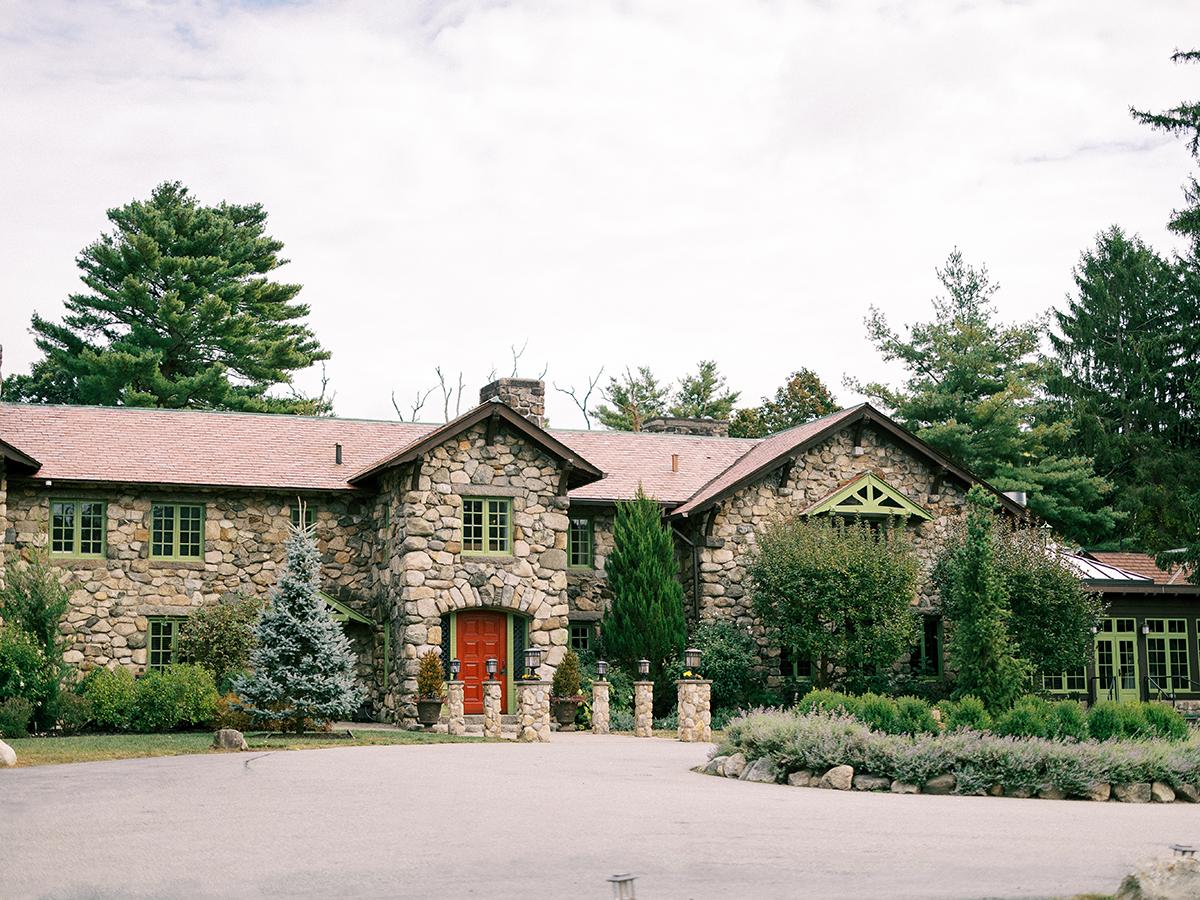 Stone house with red door, surrounded by trees and bushes.
