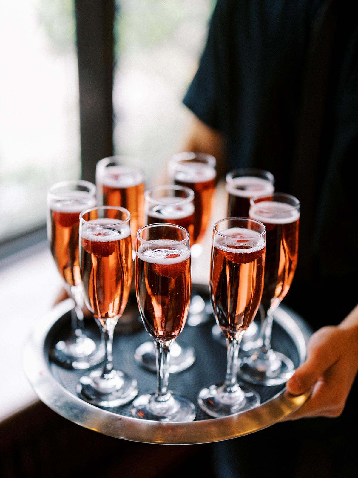 Serving tray with glasses of pink champagne garnished with berries.