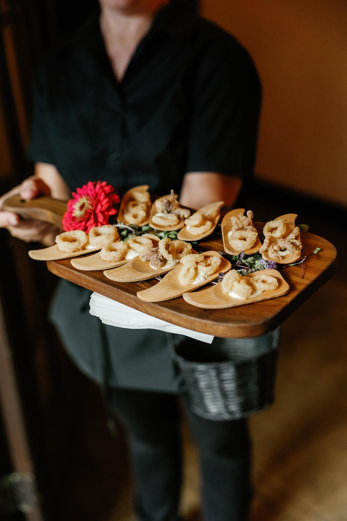 Server holding a tray of appetizers with a red flower.