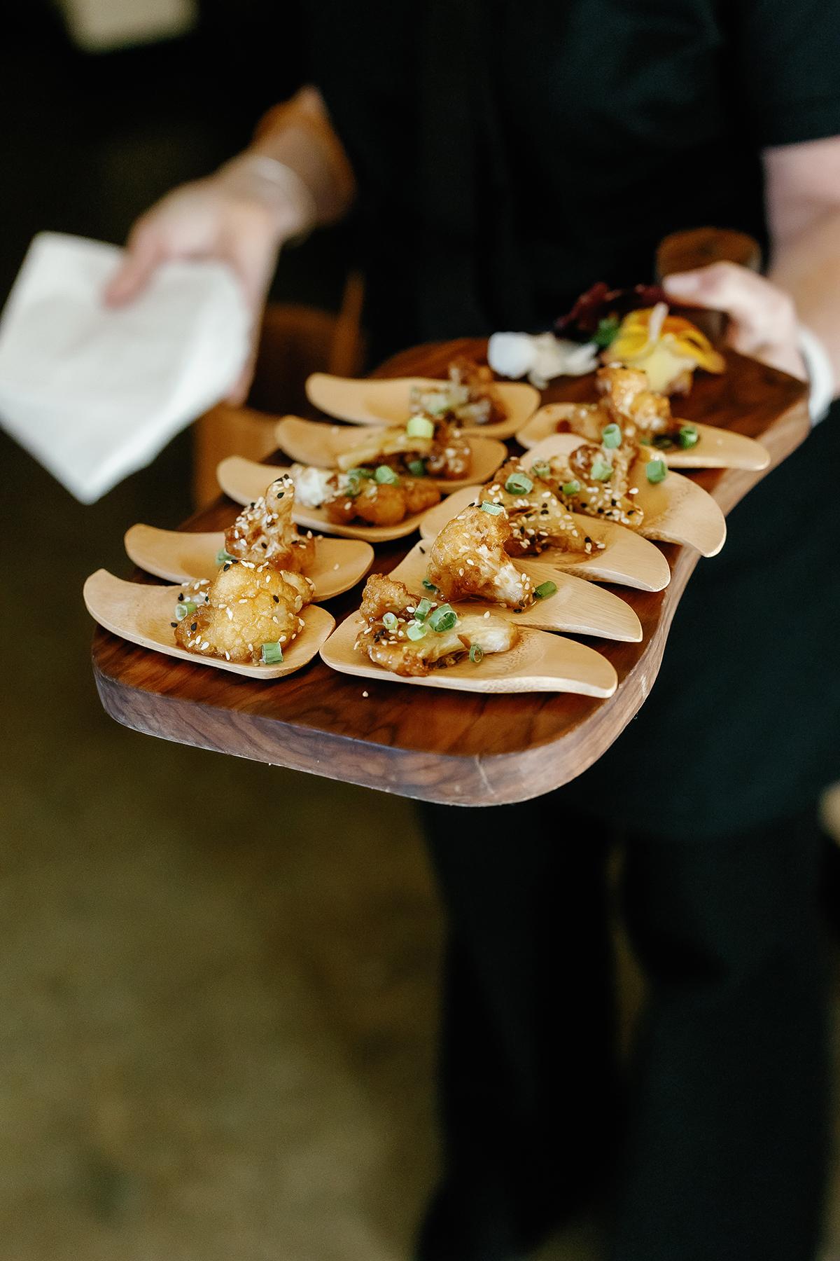 Appetizers served on a wooden platter by a person in black attire.