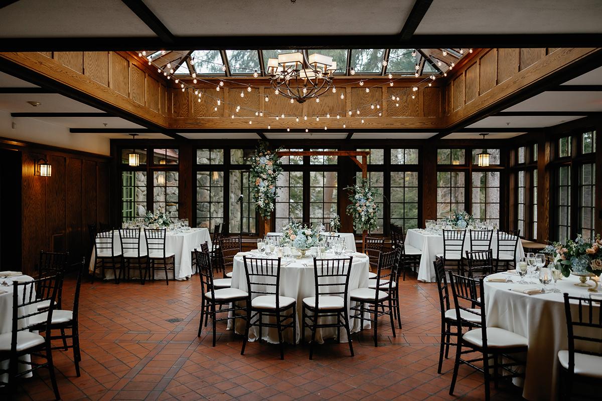 Elegant hall with round tables, white tablecloths, and string lights above.
